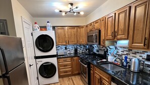 A compact kitchen with wooden cabinets, a stainless steel refrigerator, a washing machine, a microwave, and a dishwasher.