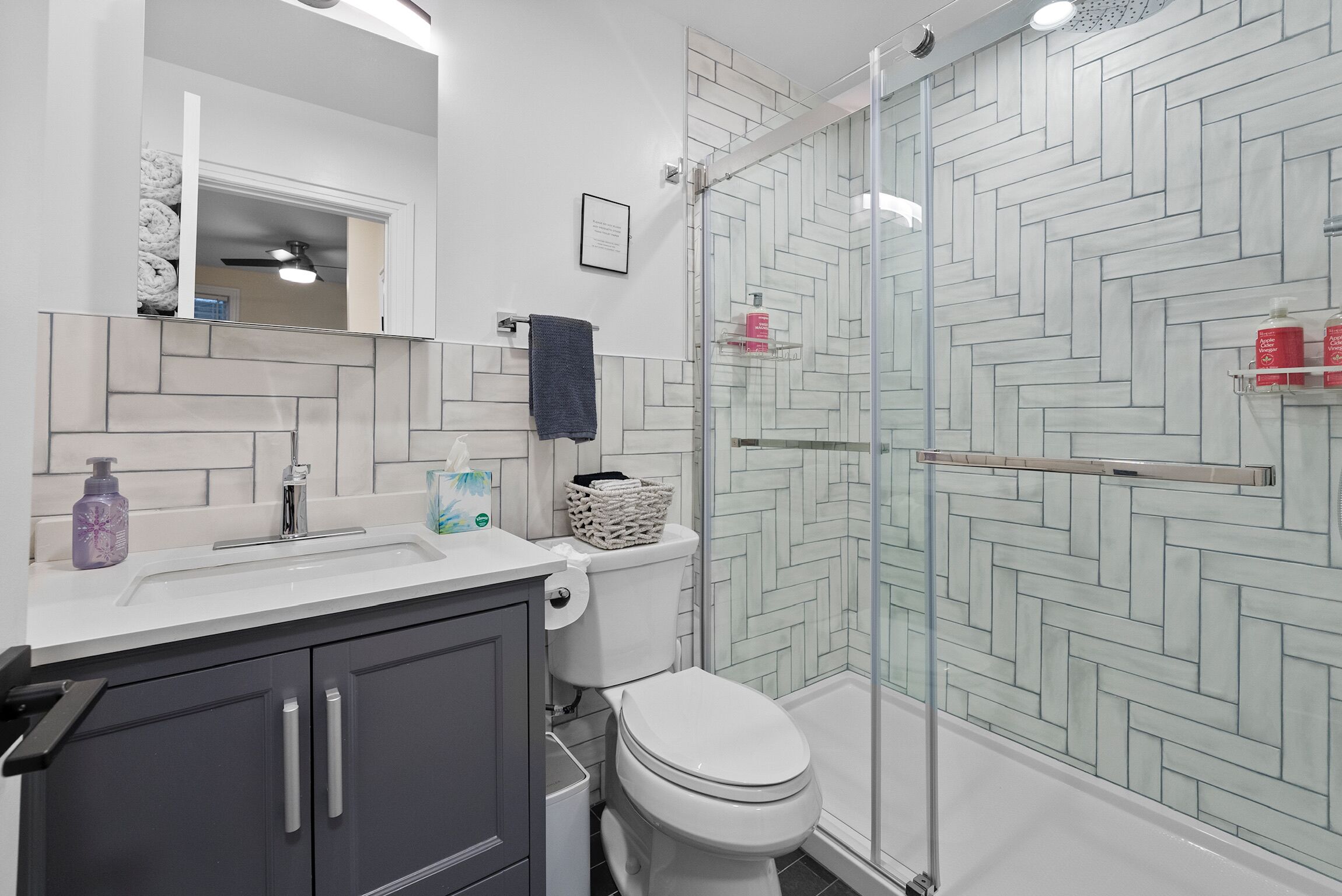 A modern bathroom with a white sink, dark cabinets, a toilet, and a glass shower enclosure.