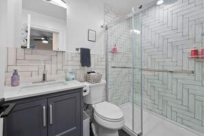 A modern bathroom with a white sink, dark cabinets, a toilet, and a glass shower enclosure.