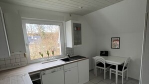 A compact kitchen with white cabinets, a window, a sink, a stove, and a dining table with chairs. - Quiet vacation apartment in the beautiful Sauerland (Meschede)