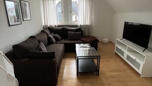 A living room with a sofa, a coffee table, a TV stand, and a ceiling fan. - Quiet vacation apartment in the beautiful Sauerland (Meschede)