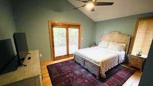 Une chambre à coucher avec un lit, un ventilateur de plafond, une télévision, un bureau en bois et un tapis à motifs.