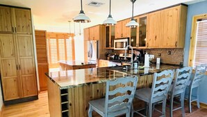 Une cuisine avec des meubles en bois, un îlot central doté de tabourets, des luminaires suspendus et un four à micro-ondes.