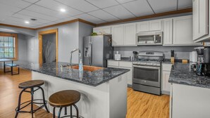 Una cocina moderna con armarios blancos, encimera de granito, electrodomésticos de acero inoxidable y suelo de madera.