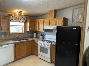 A kitchen with wooden cabinets, a white dishwasher, a stove, and a black refrigerator. - Located right off main roads - with access to fishing, boating & hunting nearby! (Dawson)