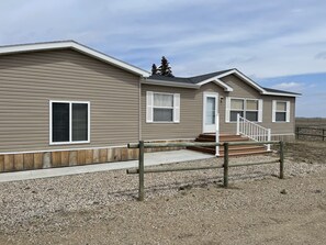 A two-story mobile home with a wooden deck and a gravel driveway. - Located right off main roads - with access to fishing, boating & hunting nearby! (Dawson)