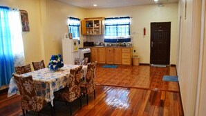 Comedor con una mesa dispuesta para cuatro, armarios de madera, zona de cocina con estufa y una puerta con extintor.
