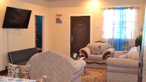 Una sala de estar con televisión de pantalla plana, dos sillones, un sofá y un tapete estampado.