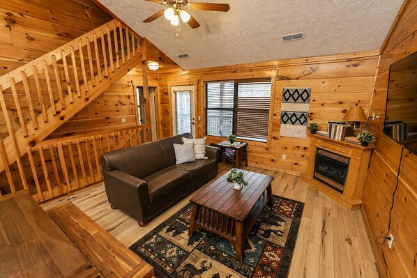 A wooden cabin interior with a staircase, a sofa, a coffee table, and a fireplace.
