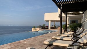 Un espace aménagé au bord de la piscine, avec des chaises longues, une petite piscine et une vue sur la mer.
