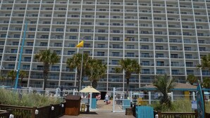 Ein mehrstöckiges Hotel mit Balkongitter, Palmen und direktem Zugang zum Strand.