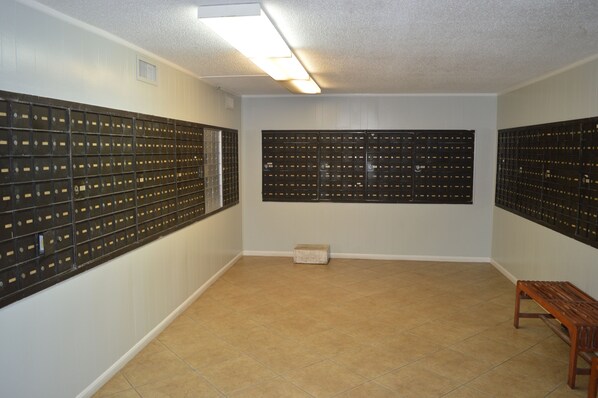 A room with a tiled floor, a bench, and a wall with multiple mailboxes.