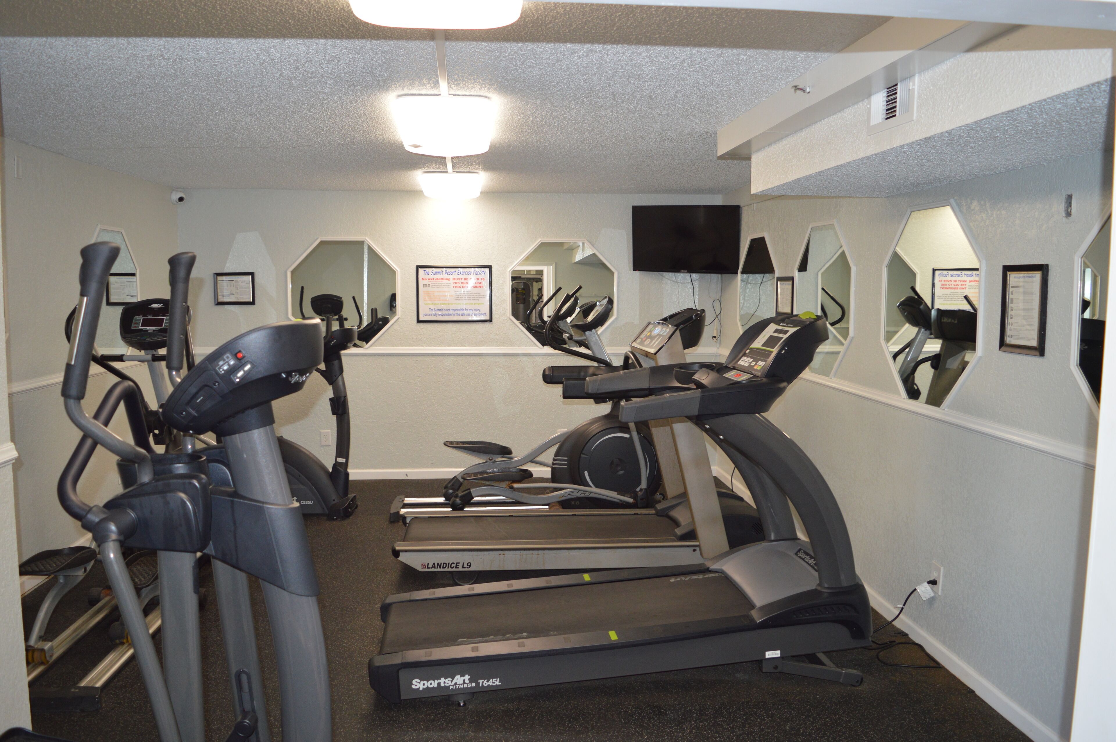 A gym with treadmills, ellipticals, and a TV on the wall.