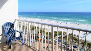 Ein Balkon mit Blick auf einen Strand, einem Stuhl und einem Spielbereich mit Sonnenschirmen und Personen.