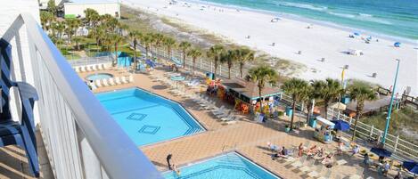 A hotel pool area with multiple pools, beach view, and beach amenities.