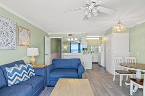 A living room with a blue sofa, a wooden coffee table, and a dining area with white chairs and a wooden table.
