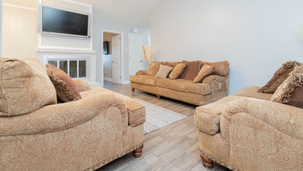A living room with two patterned sofas, a flat-screen TV mounted above a fireplace, and a ceiling fan.