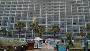 Een hotel met meerdere verdiepingen, een rij van balkons, palmbomen en toegang tot het strand.