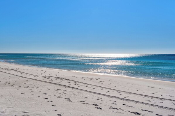 Une plage où l’on voit des empreintes de pas menant à l’eau, un ciel dégagé et l’océan.