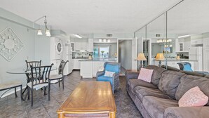 Un salon spacieux avec un canapé en cuir marron, une table basse en bois et un coin repas comprenant une table et des chaises en verre.