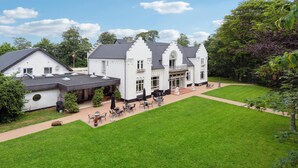 Een groot wit gebouw met een ruime patio, meerdere eettafels en een verzorgd gazon.
