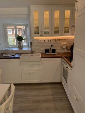 Una cocina moderna con armarios blancos, una encimera de madera y una ventana con vistas a edificios.