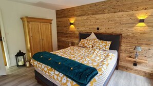 A bedroom with a wooden headboard, a bed with a yellow and white floral bedspread, a teal throw blanket, and two wall-mounted lamps. - Allegra Appenzell (Trogen)