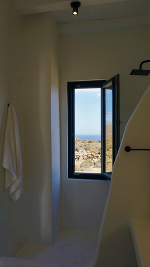 Ein Badezimmer mit Fenster und Blick auf eine felsige Landschaft und das Meer.