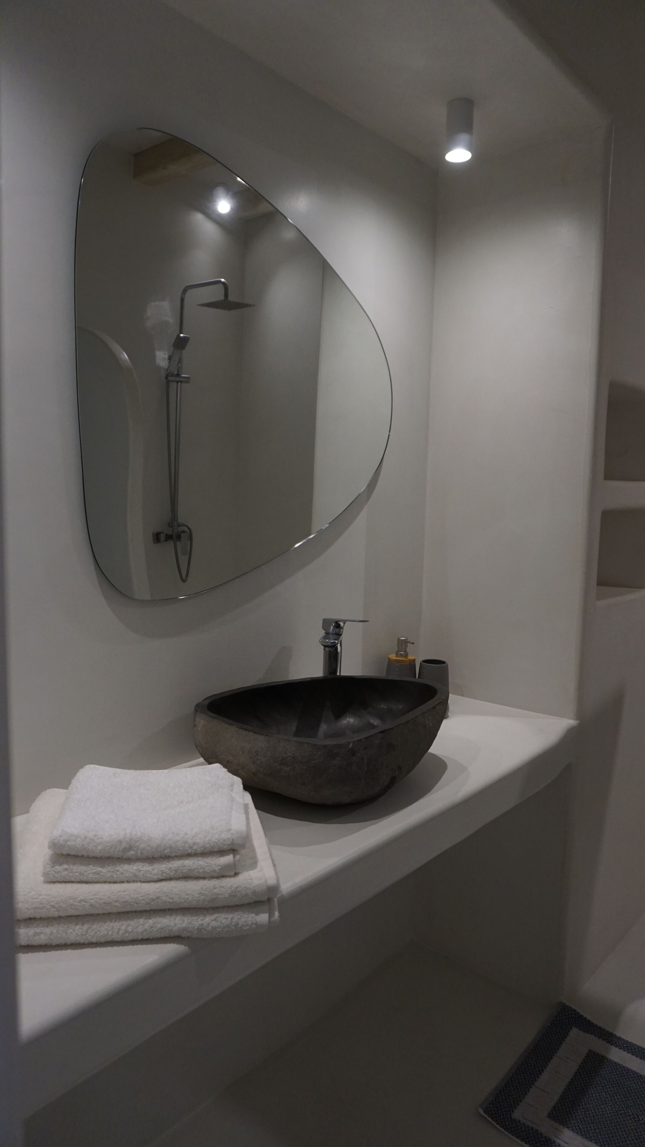 Un baño con un espejo grande, un lavamanos redondo y un perchero para toallas.