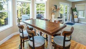 A dining area with a wooden table and four chairs, large windows, and a view of the outdoors. - Sopra Bella- Elegant 4BR, Family Friendly, OSU (Corvallis)