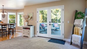 A spacious living room with a large sliding glass door leading to an outdoor patio. There is a dining area with wooden chairs and a white cabinet. - Sopra Bella- Elegant 4BR, Family Friendly, OSU (Corvallis)
