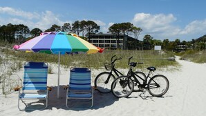 Une plage avec deux chaises de plage à rayures, un parasol coloré et deux vélos.
