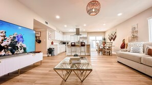A modern living room with a glass coffee table, a TV, a sofa, and a dining area with chairs and a table.
