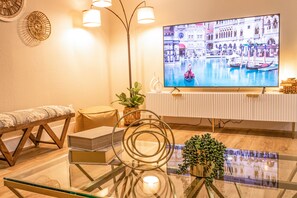 A modern living room with a glass coffee table, a sofa, a TV displaying a canal scene, and a radiator.