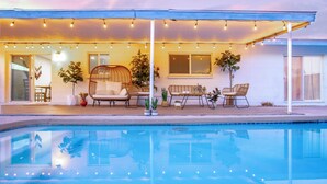 Zona de piscina con mobiliario exterior, luces colgantes y plantas en macetas.