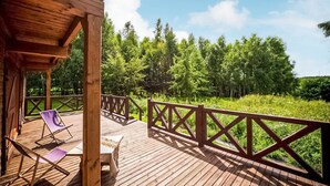 A wooden deck with a railing, two lounge chairs, and a view of a forested area. - Cozy apartment in KLECINO with lake view (KLECINO)