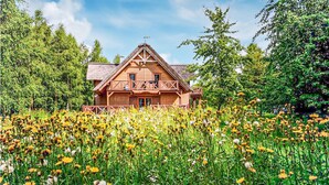 A wooden cabin with a balcony, surrounded by a field of wildflowers and trees. - Cozy apartment in KLECINO with lake view (KLECINO)