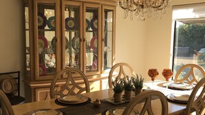 A dining area with a wooden table set for four, surrounded by matching chairs. A glass-fronted china cabinet is visible in the background.