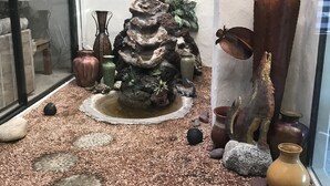 A small indoor garden with a rock waterfall, decorative vases, and a wooden sculpture.
