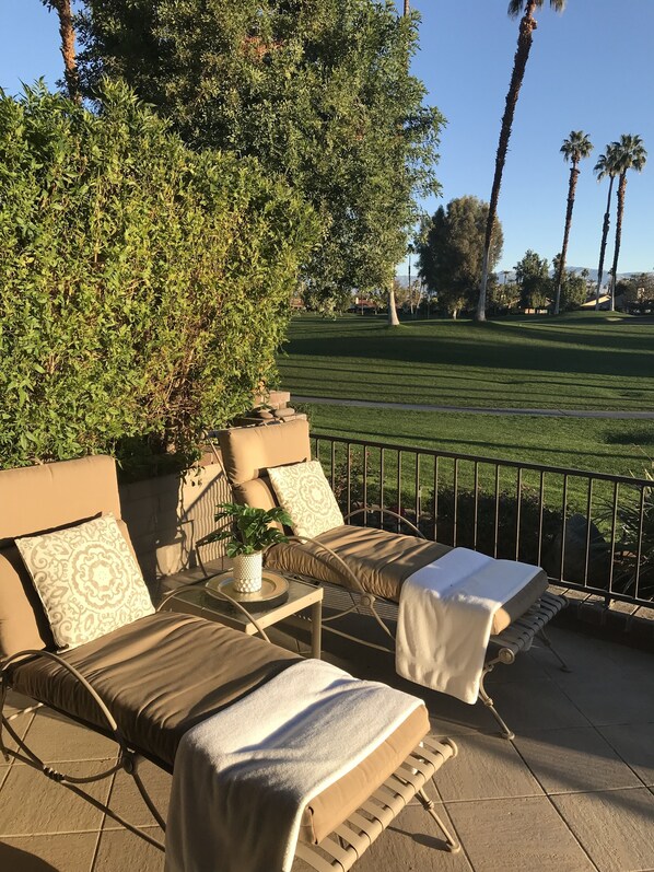 Een terras met twee comfortabele stoelen, een tafeltje met een plant en uitzicht op een golfbaan.