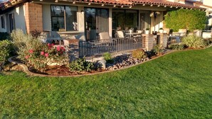 A house with a tiled roof, a covered patio with outdoor furniture, and a well-maintained garden with various plants and flowers.