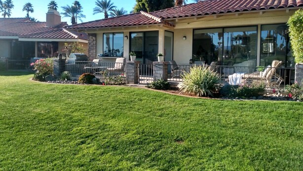 A two-story house with a patio area, a barbecue grill, and a well-maintained lawn.