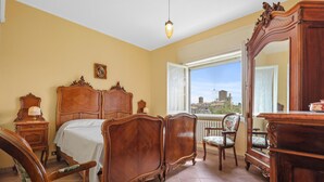 Un dormitori amb un llit gran, una cadira, una petarrera i una finestra amb vista a una ciutat.