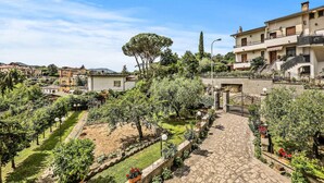 Zona residencial amb un camí pavimentat, vegetació abundant i un edifici de diverses plantes amb balcons.