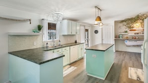 Une cuisine moderne avec des meubles de couleur bleu clair, un plan de travail en granit et un lustre.