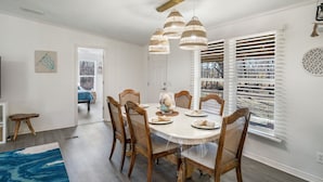 Un espace repas comprenant une table ronde, six chaises en bois et un luminaire suspendu au plafond.