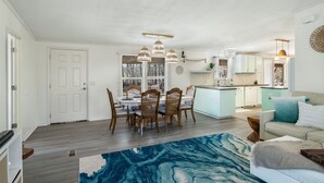 Un vaste espace de vie comprenant une table à manger et des chaises, une cuisine à l’arrière-plan et un tapis bleu à motifs.