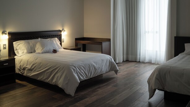 Habitación de hotel con una cama grande, una mesita de noche, un escritorio y una ventana con cortinas.