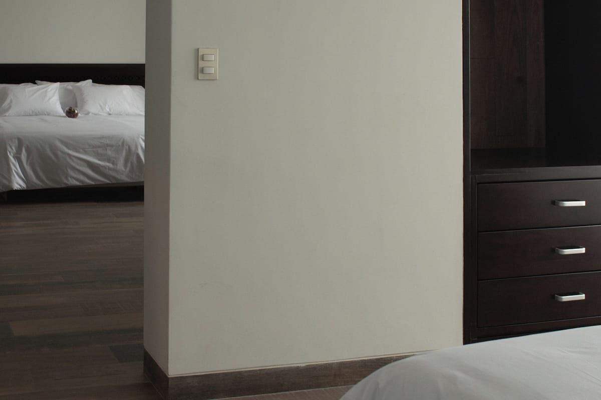 Ein Hotelzimmer mit Bett, Nachttisch, Kommode und Lichtschalter.