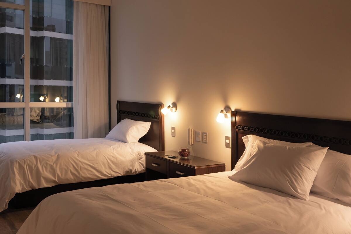 Ein Hotelzimmer mit zwei Betten, einem Nachttisch mit Lampe und einem Fenster mit Vorhängen.